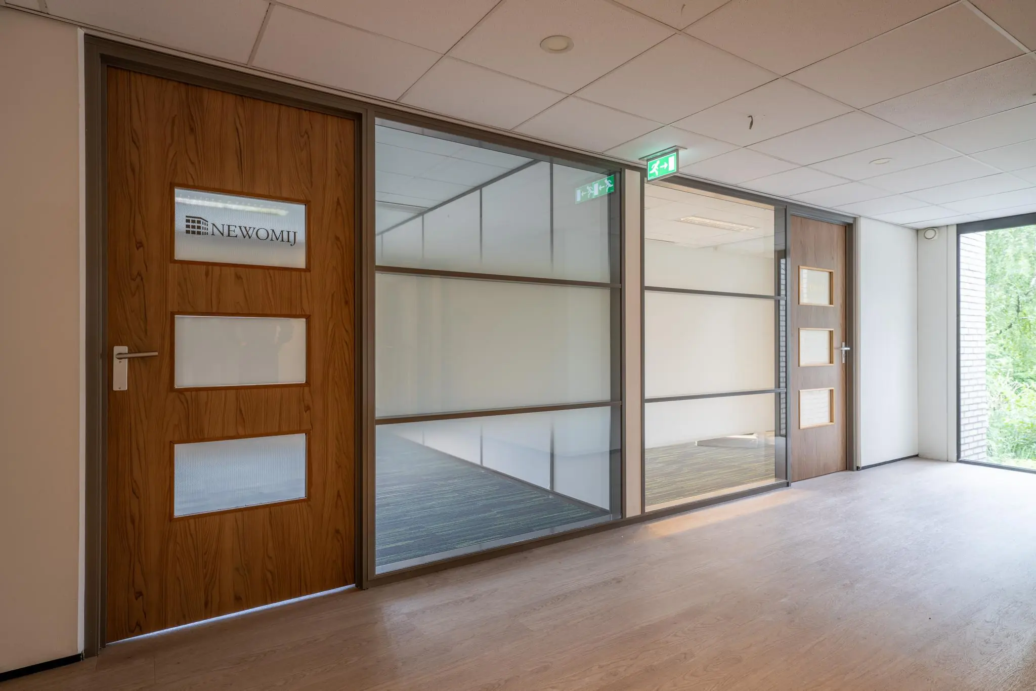Moderne kantoorruimte met houten deuren en glazen wanden in het gebouw aan de Burgemeester Verderlaan, met zicht op het kantoor van Newomij.